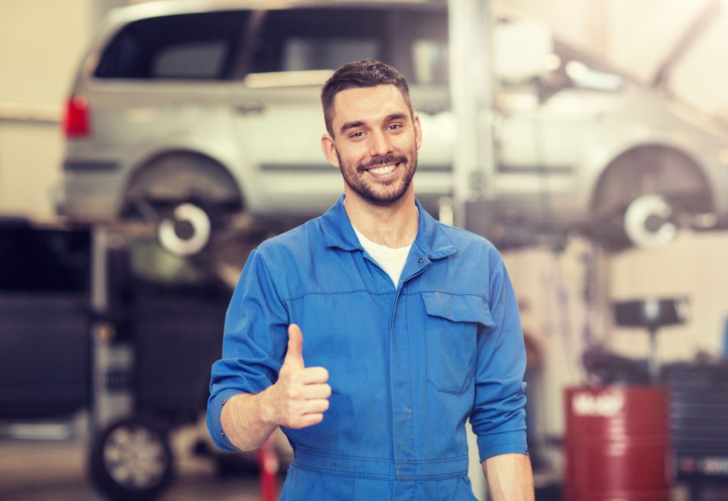 Un mecánico con su traje azul, sonriendo con el dedo pulgar levantado